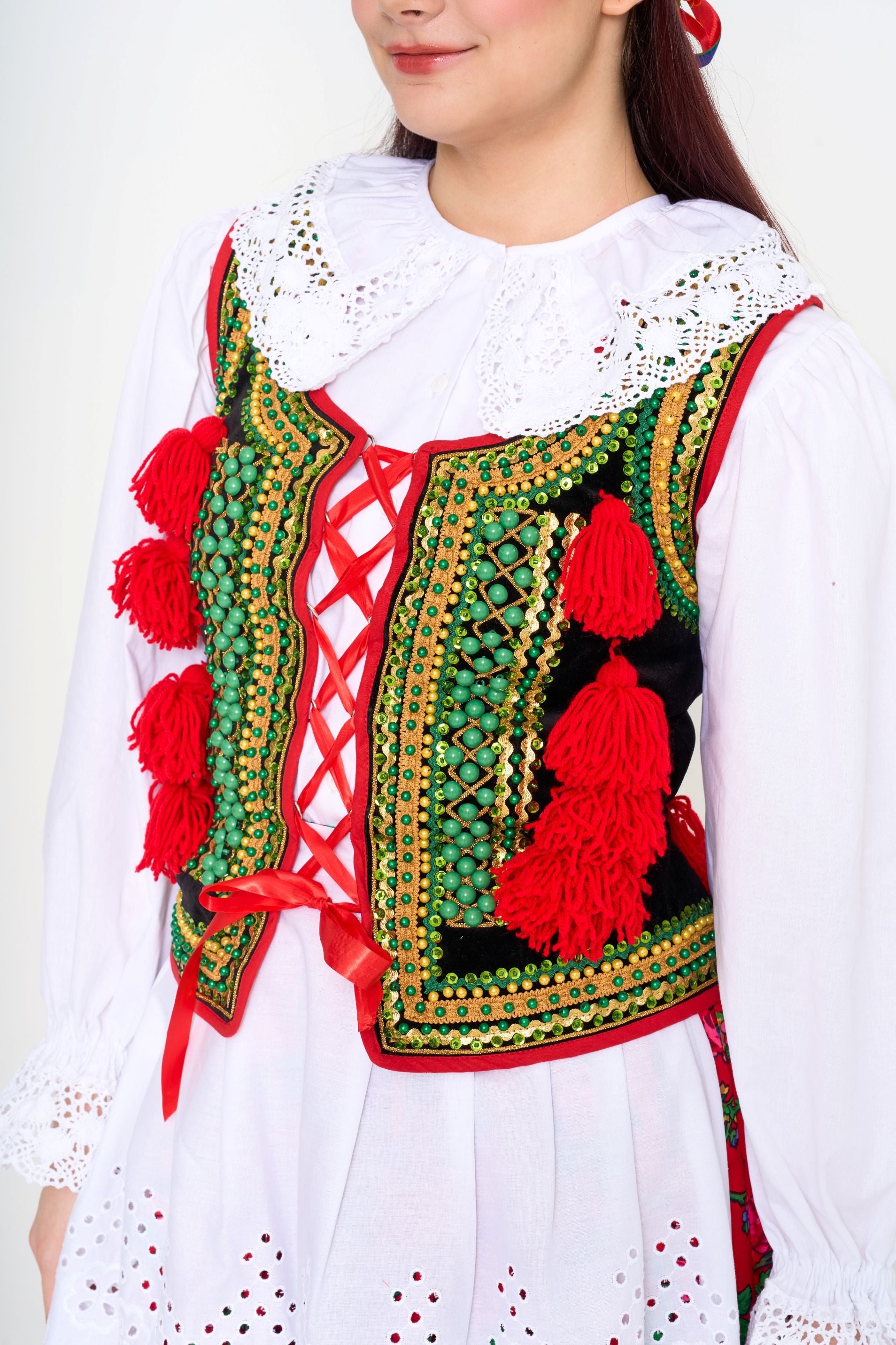 Close-up detail of the embroidered vest, highlighting the green and red hues and playful red pom-poms.