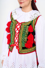 Close-up detail of the embroidered vest, highlighting the green and red hues and playful red pom-poms.